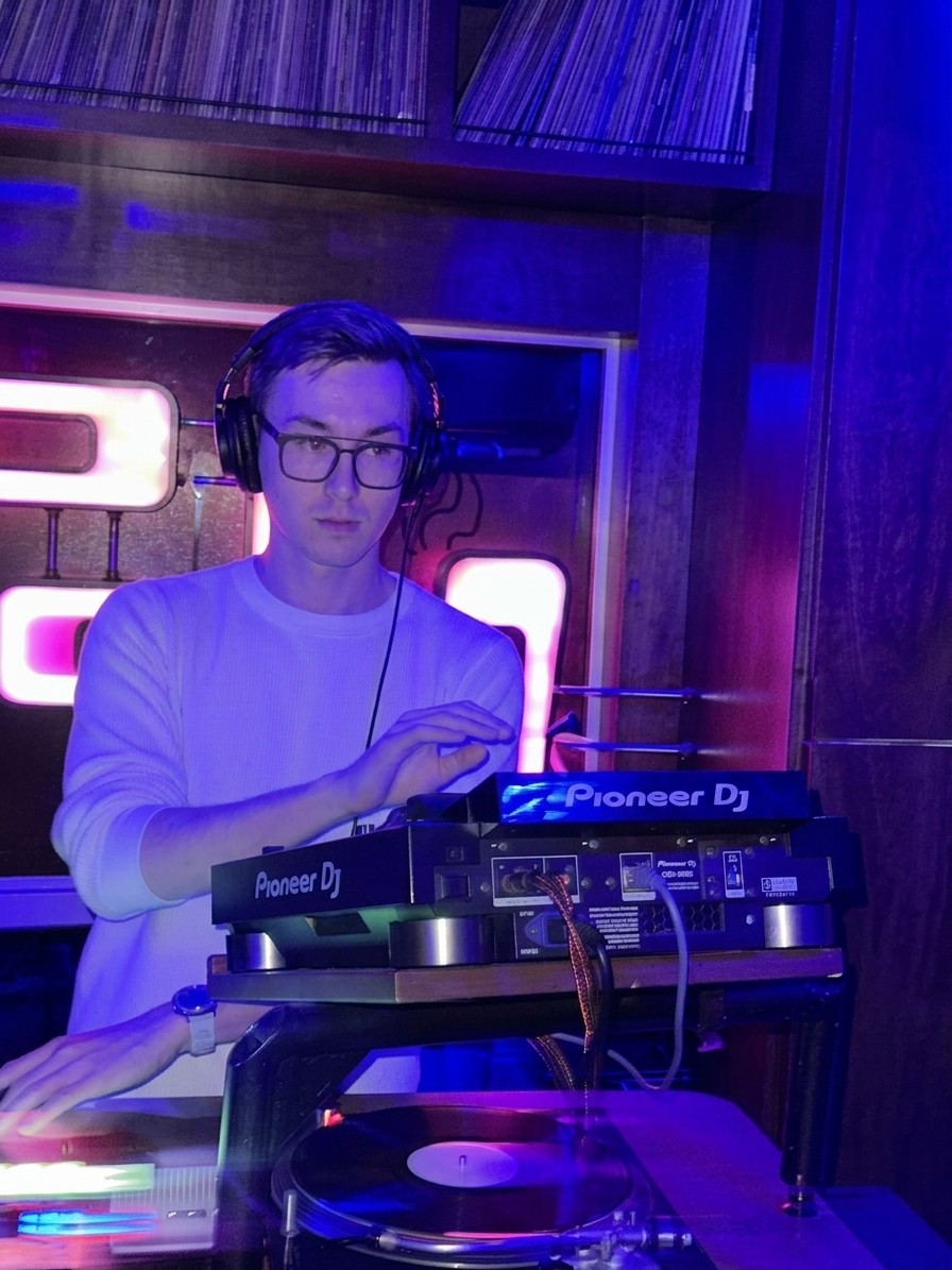 Chris Ryo DJing on Pioneer decks and a turntable under violet club lights